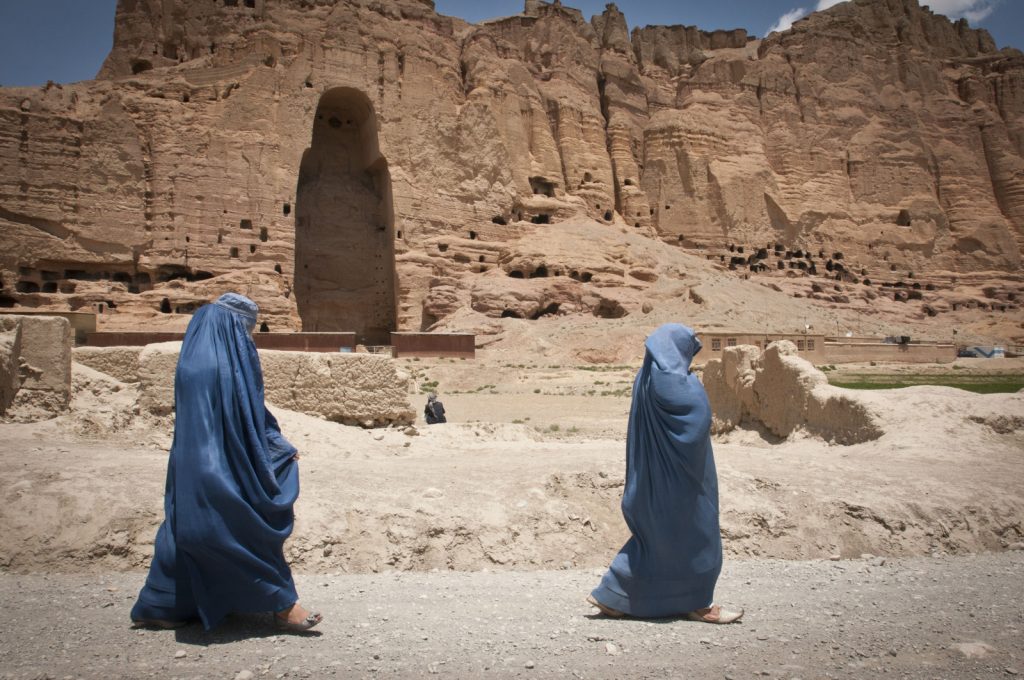 Two women walk past the huge cavity where one of the ancient Buddhas of Bamiyan, known to locals as the "Father Buddha," used to stand, June 17, 2012. The monumental statues were built in A.D. 507 and 554 and were the largest statues of standing Buddha on Earth until the Taliban dynamited them in 2001.